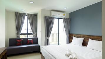 A hotel room with a bed, a sofa, and a window with curtains.