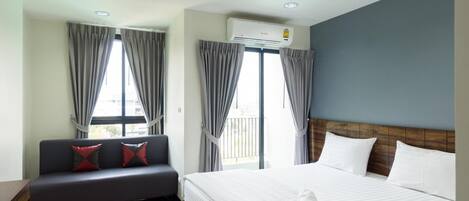 A hotel room with a bed, a sofa, and a window with curtains.