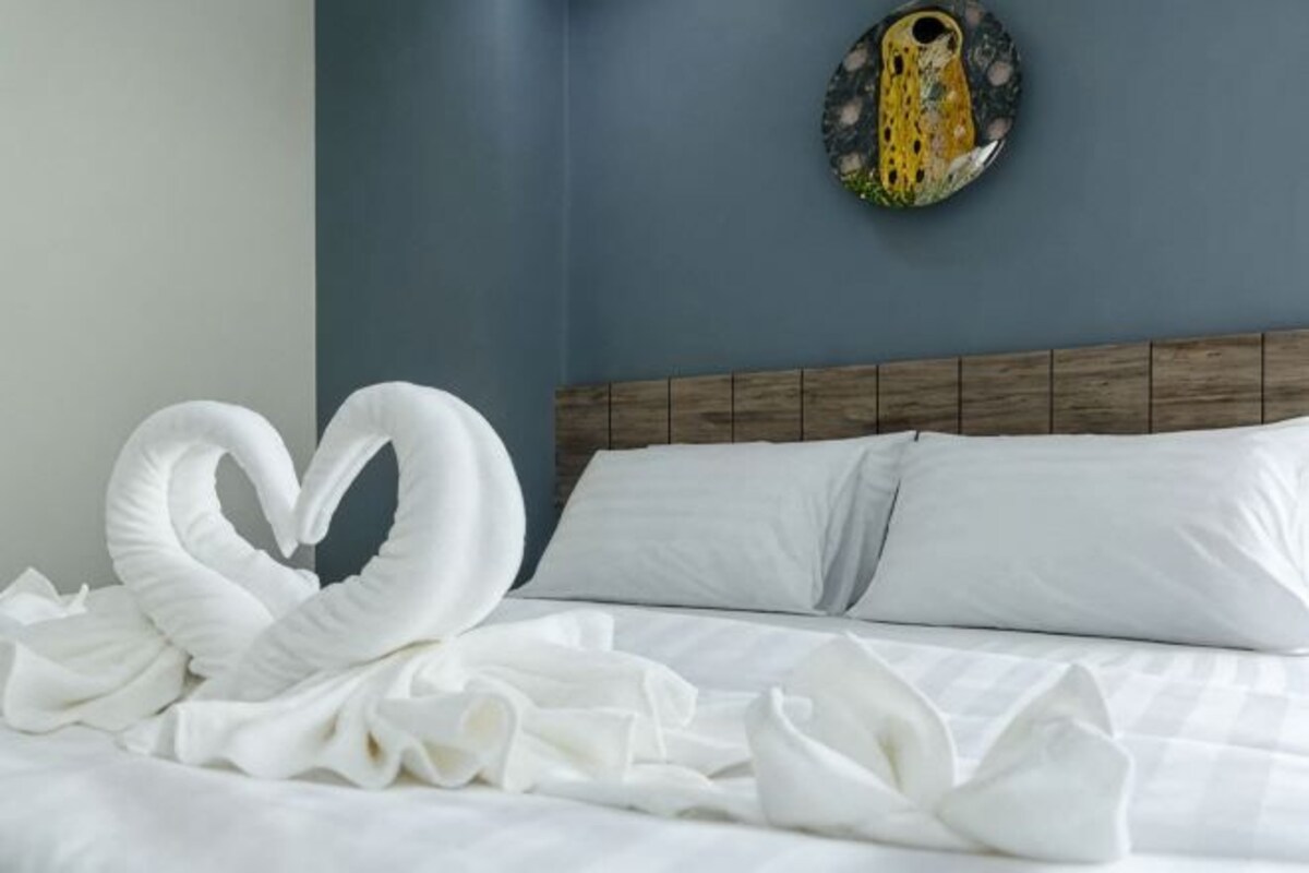 A bed with white linens and a heart-shaped towel arrangement.