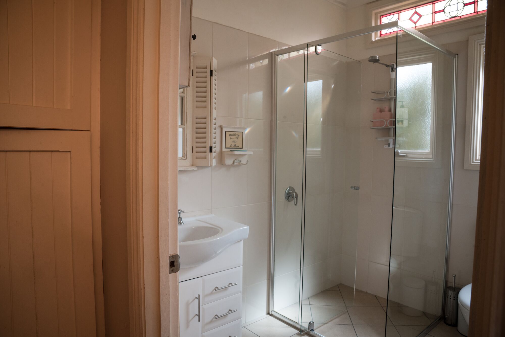 A modern bathroom with a glass shower enclosure, a white sink, and a vanity with drawers.