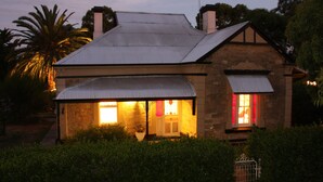 A stone house with a metal roof, two lit windows, and a visible chimney. - Azalea Cedar-Rose Villa (Lyndoch)