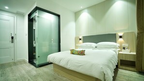 Un dormitori modern amb un llit gran, un armari amb portes de vidre i taules de nit integrades amb làmpades.