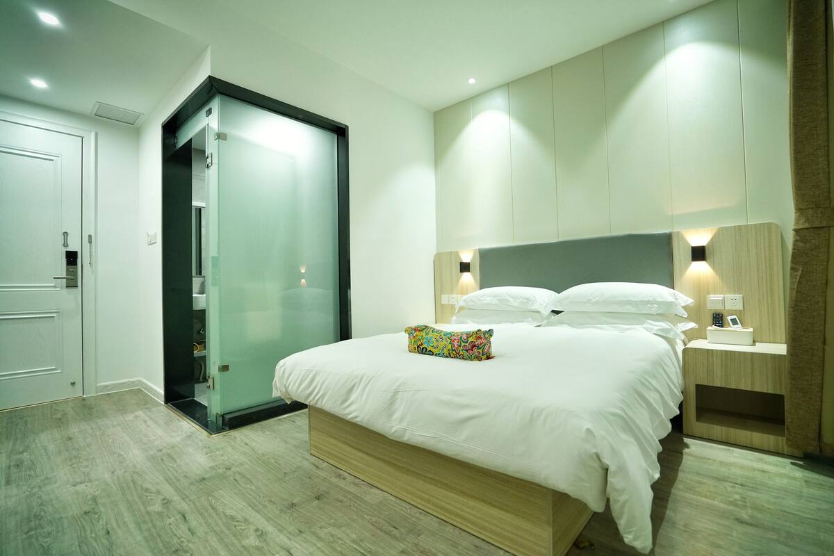 Ein modernes Schlafzimmer mit einem großen Bett, einem Schrank mit Glastüren und integrierten Nachttischen mit Lampen.