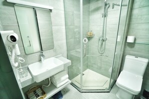 A modern bathroom with a glass-enclosed shower, a white sink, a mirror, and a toilet. - Hengdian Chayan Guest House (Jinhua)