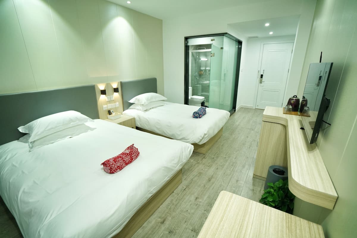 Ein Hotelzimmer mit zwei Betten, einer Dusche, einem WC, einem Fernseher und einer kleinen Schreibtischzeile.