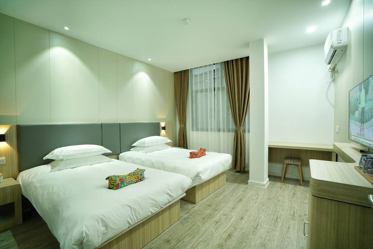 Ein Hotelzimmer mit zwei Betten, einem Schreibtisch, einem Sessel, einem Fernseher und einer Klimaanlage.