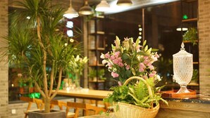 Interior de restaurant amb taules i cadires de fusta, una planta gran en test i un lluernari de vidre decoratiu.