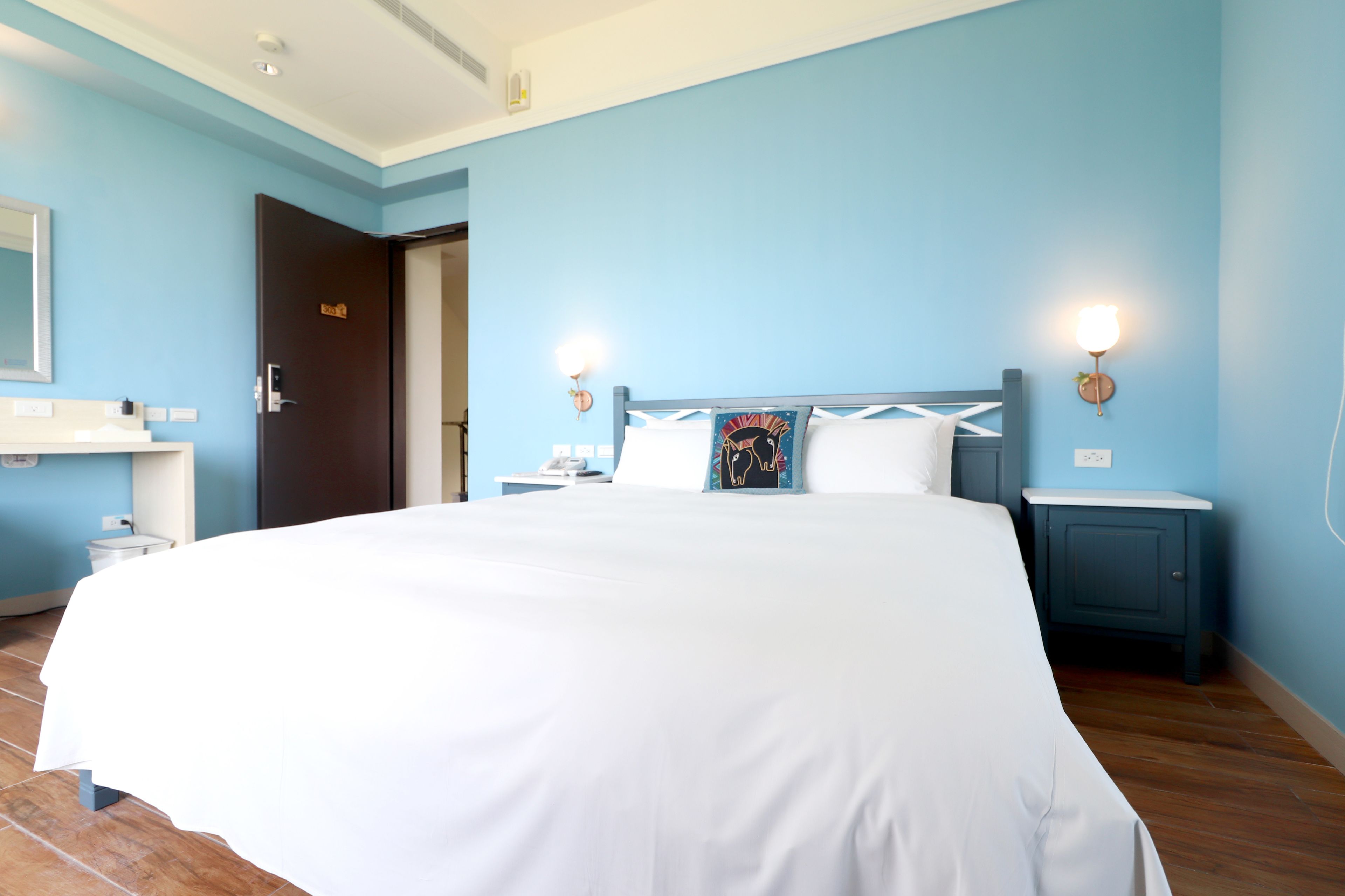 Ein Hotelzimmer mit einem großen Bett, einem Nachttisch, einem Spiegel und einer Tür.