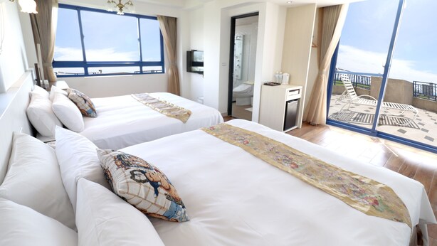 Une chambre d’hôtel avec deux lits, une grande fenêtre, un balcon et une salle de bain visible par une porte ouverte.