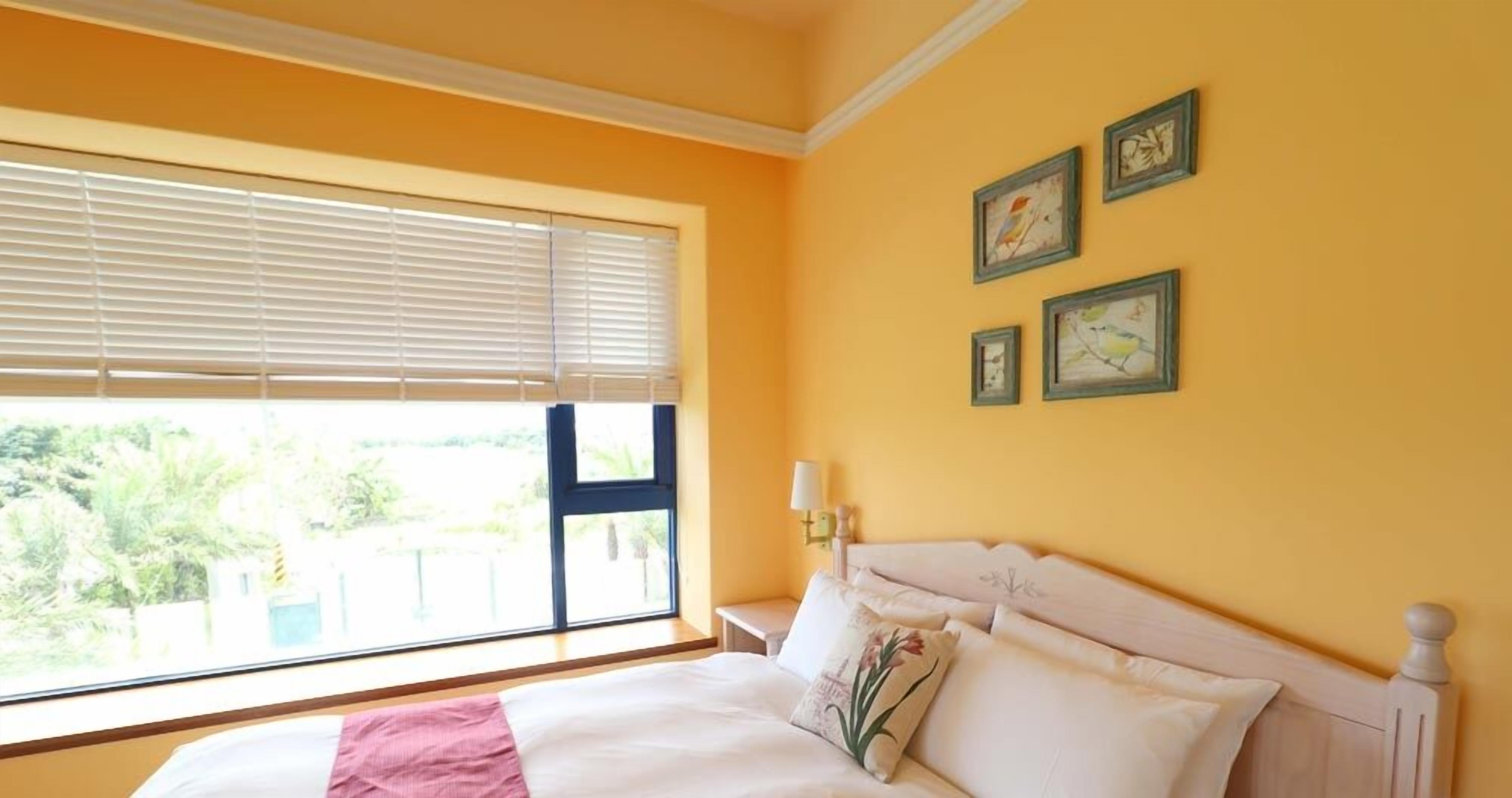 A bedroom with a bed, a window with blinds, and three framed pictures on the wall.
