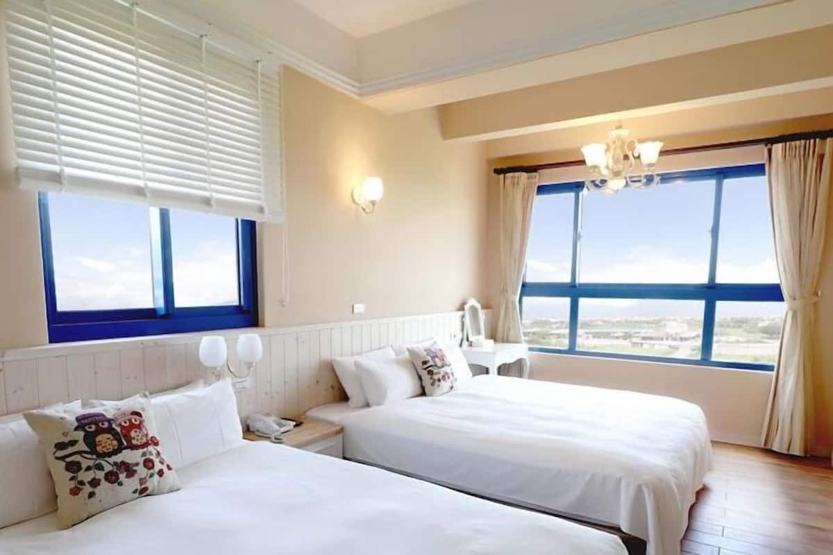A hotel room with two beds, a large window with a view, a chandelier, and a wall-mounted light.