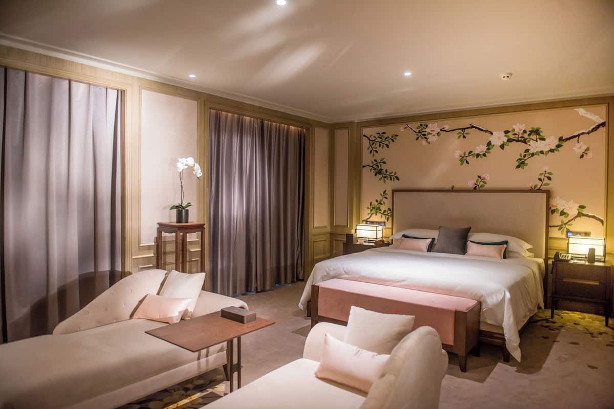 A hotel room with a large bed, two bedside tables, a sofa, a chair, and a small table with a lamp.