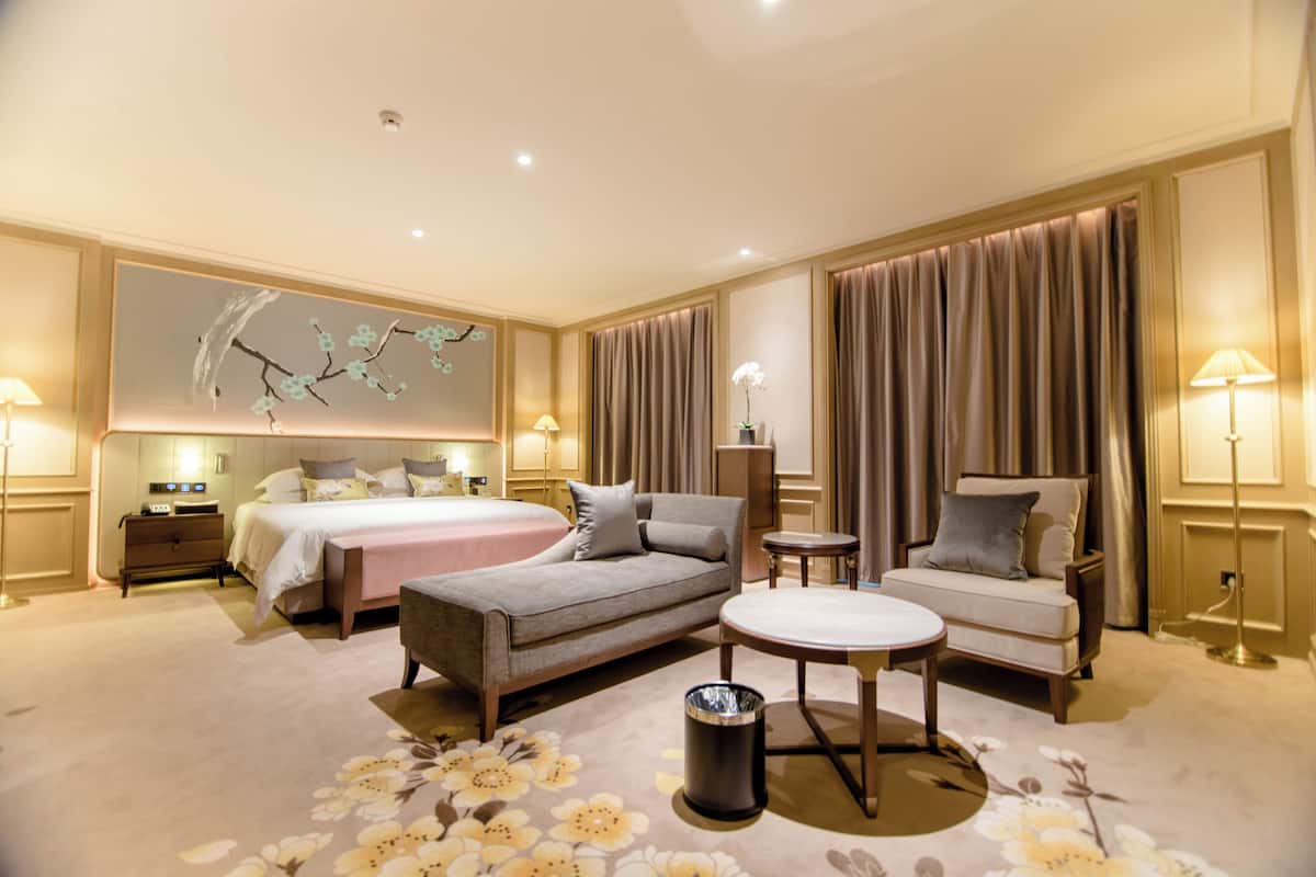 A hotel room with a large bed, two sofas, a small table, and a decorative wall painting.