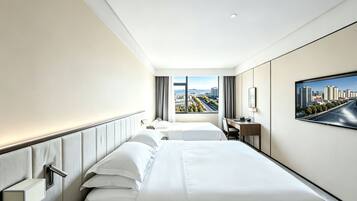 Habitación de hotel con dos camas, un escritorio, una silla, un televisor y ventana con vista a la ciudad.