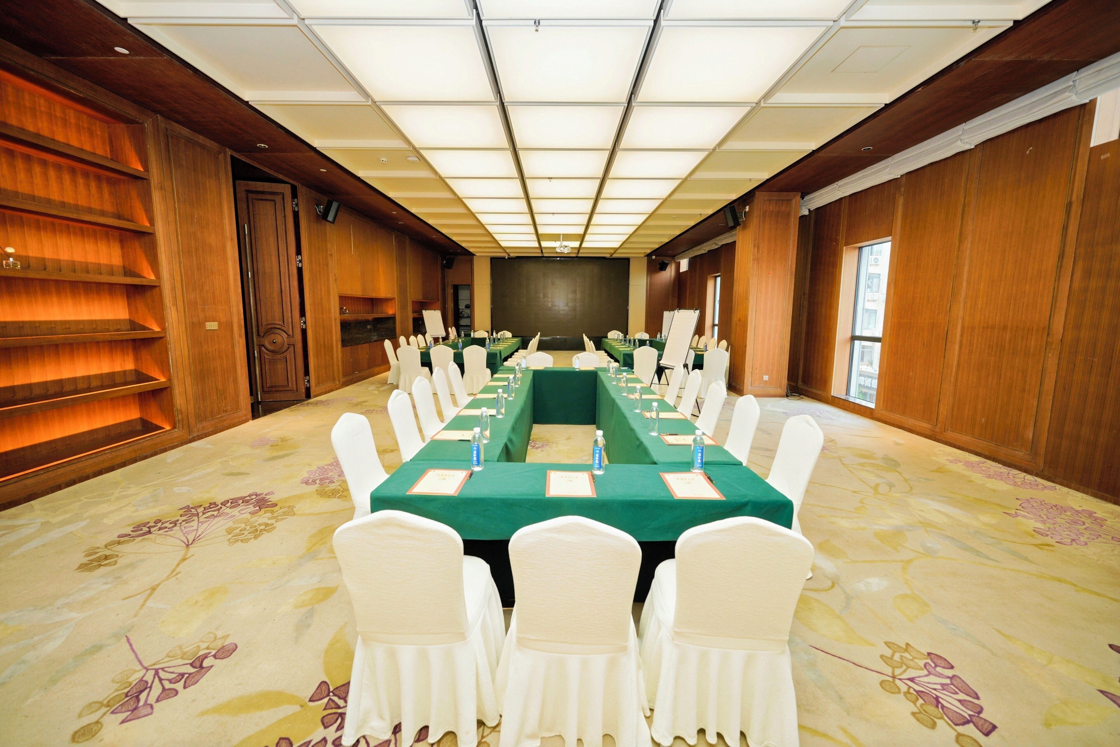 Un salón de conferencias con una larga mesa, sillas blancas y un mantel verde.