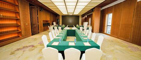 Un salón de conferencias con una larga mesa, sillas blancas y un mantel verde.