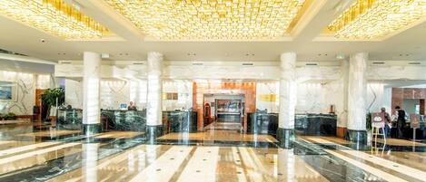 A spacious lobby with marble floors, large columns, and a patterned ceiling.