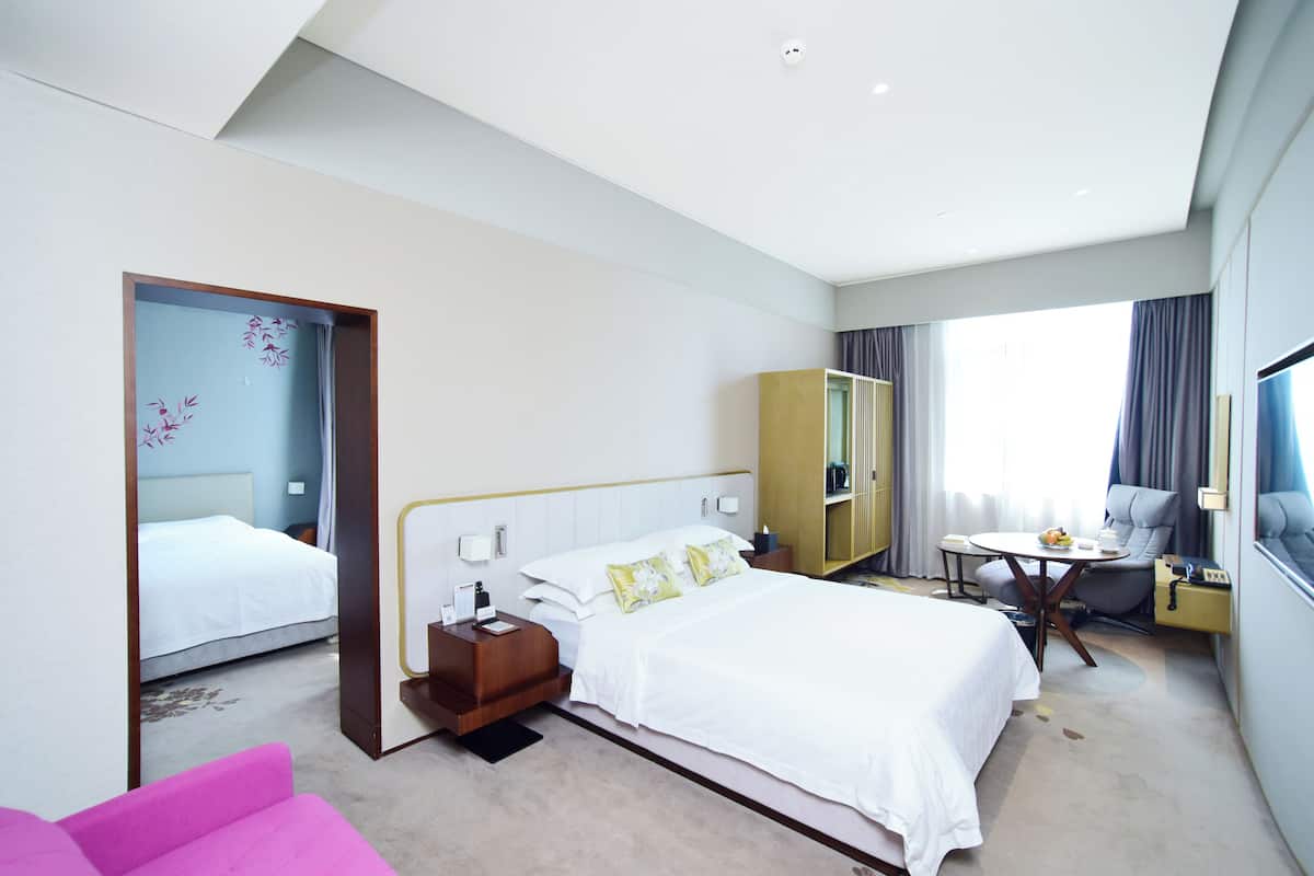 A modern hotel room with a large bed, a desk, a chair, and a wardrobe.