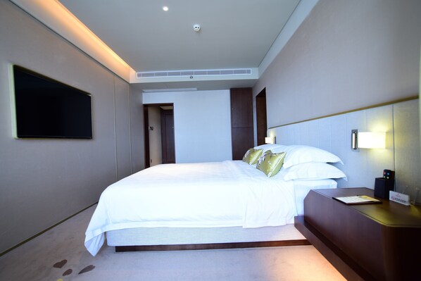 A hotel room with a large bed, a bedside table, a flat-screen TV mounted on the wall, and a door leading to another room. - Weihaiwei Hotel (Weihai)