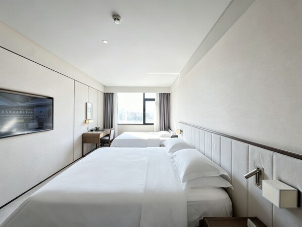 A hotel room with two beds, a desk, a chair, a TV, and a window with curtains.