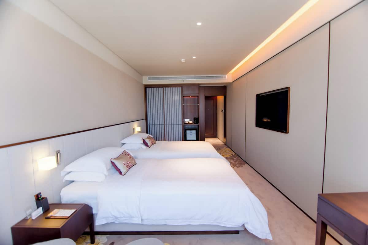 A hotel room with two beds, a desk, a chair, a TV, and a wardrobe.