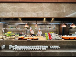 A commercial kitchen with chefs preparing food, stainless steel appliances, and neatly arranged food items.