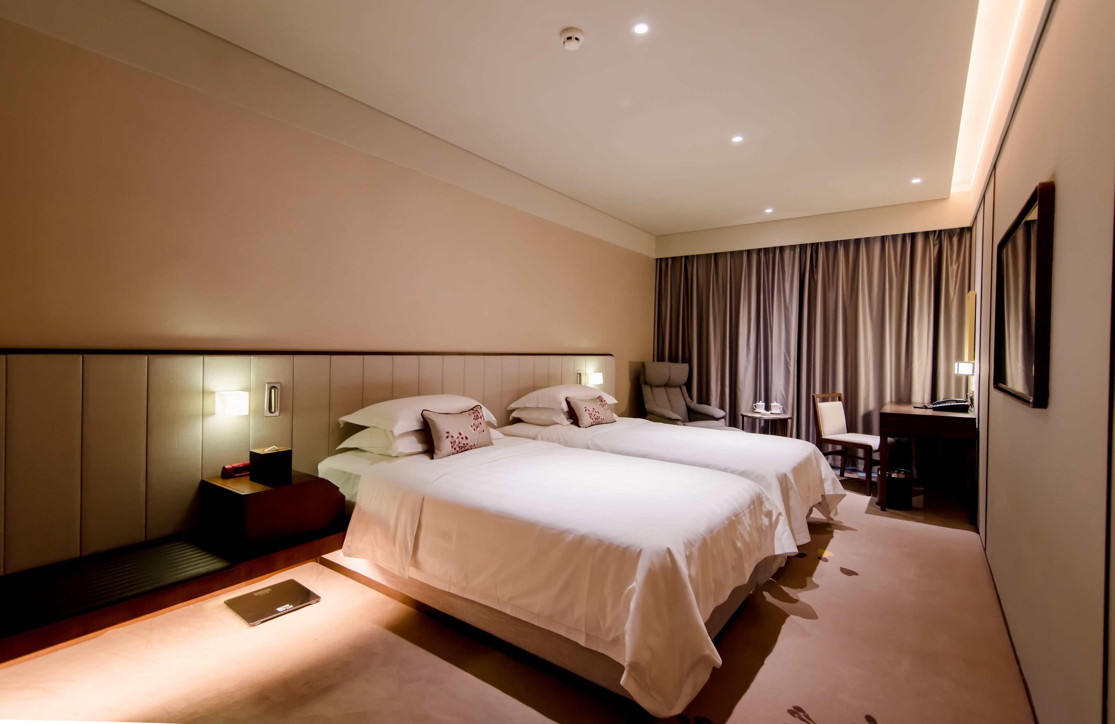 A hotel room with two beds, a desk, a chair, and a large window with curtains.
