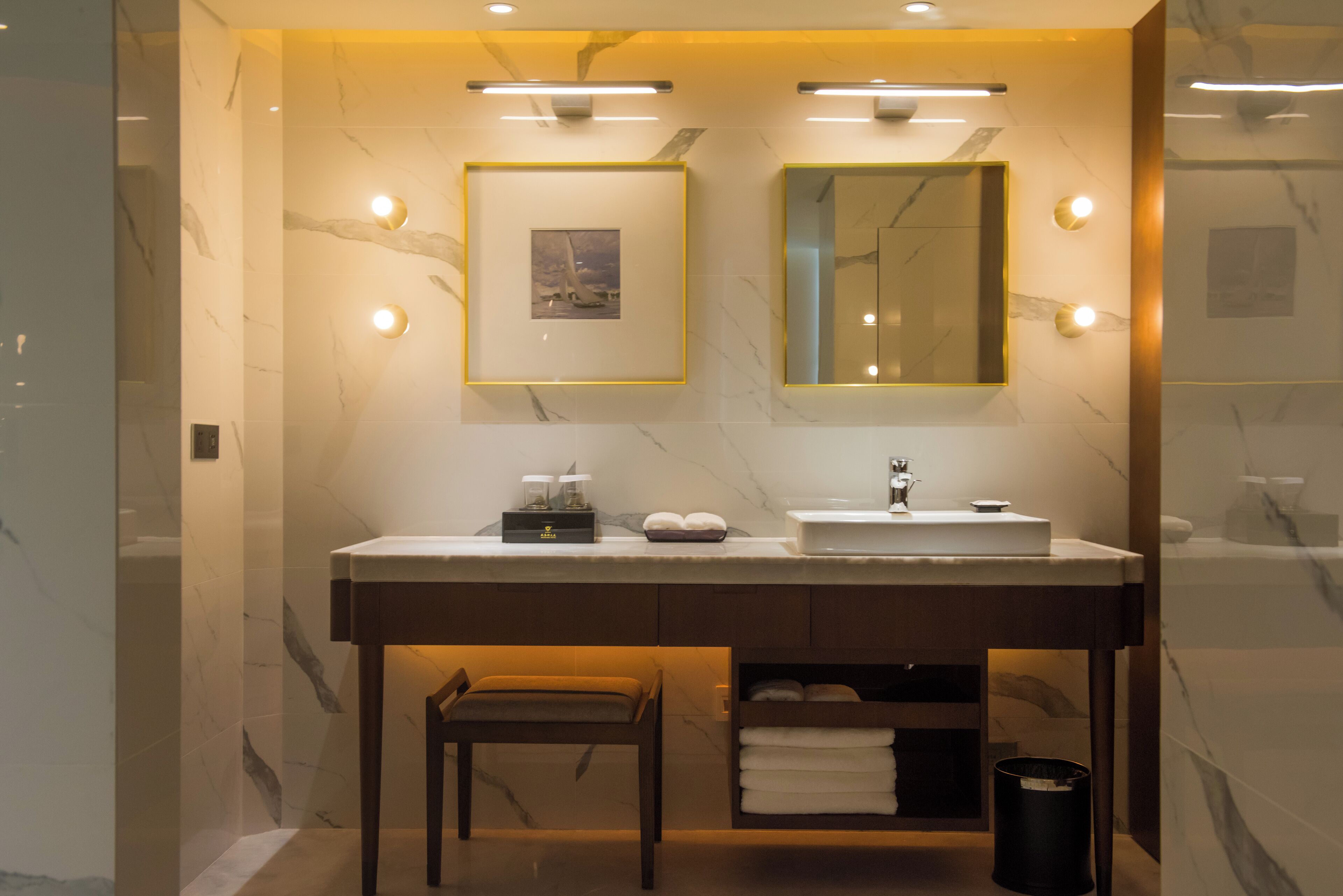Une salle de bain moderne avec un mur en marbre, un meuble-lavabo avec un évier, un miroir et une petite table avec une chaise.
