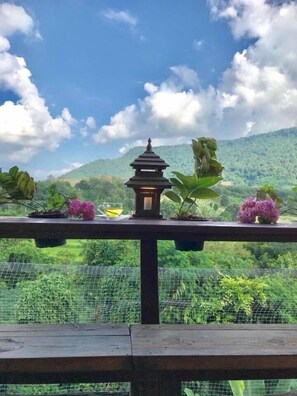 Un balcón con un farol tradicional, plantas en macetas y vistas de un paisaje verde exuberante.