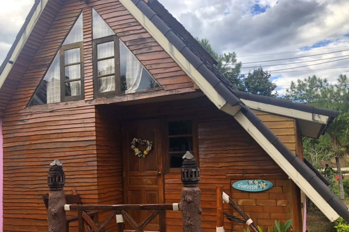 Uma cabana de madeira com telhado inclinado, porta com grinalda e um pequeno alpendre.