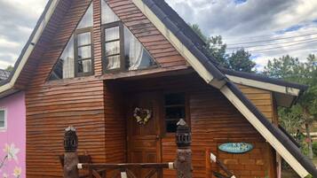 Una cabaña de madera con techo inclinado, una puerta principal con un adorno y un pequeño porche.