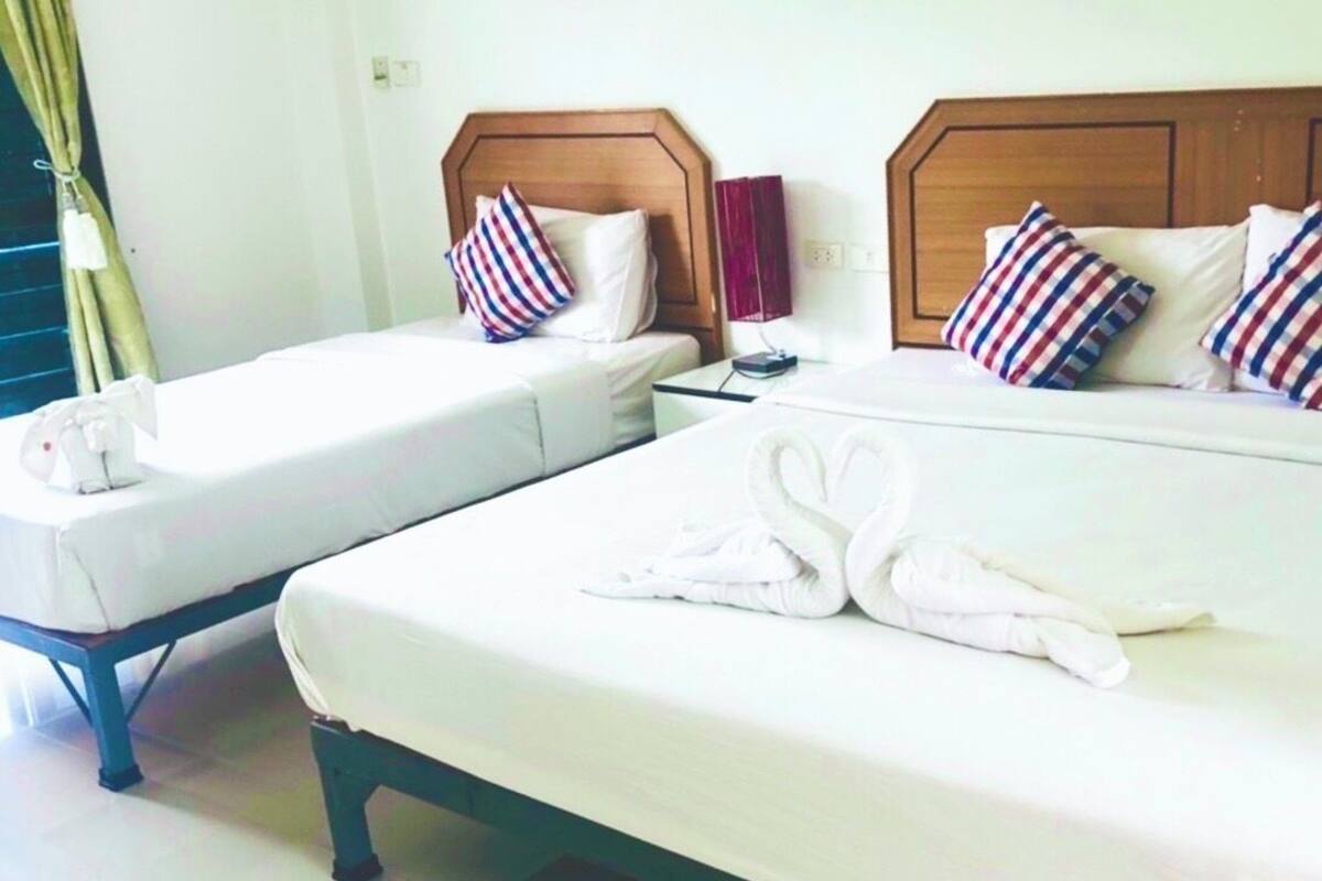 Quarto de hotel com duas camas, cada uma com roupa de cama branca e almofadas listradas. Há um par de toalhas na cama maior.