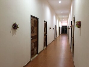 A long, narrow hallway with doors on both sides, some with decorative panels, and small floral arrangements on the walls. - Phurua Bussaba Resort & Spa (Phu Ruea)