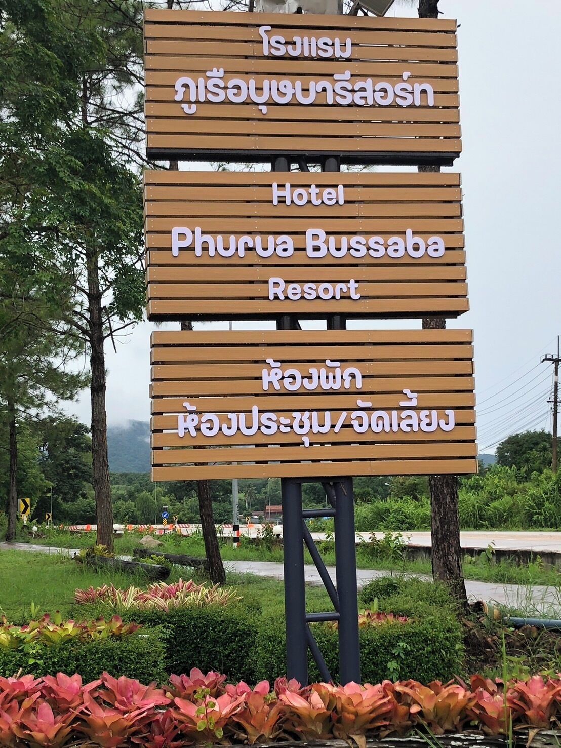 Un letrero de madera con texto que indica un hotel llamado 'Phurua Bussaba Resort', con vistas a la vegetación circundante.
