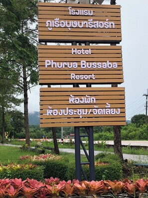 Un letrero de madera con texto que indica un hotel llamado 'Phurua Bussaba Resort', con vistas a la vegetación circundante.