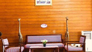 Una habitación con paneles de madera, un sofá a cuadros, dos sillones, una pequeña mesa con una planta en maceta y una estatua de jirafa.