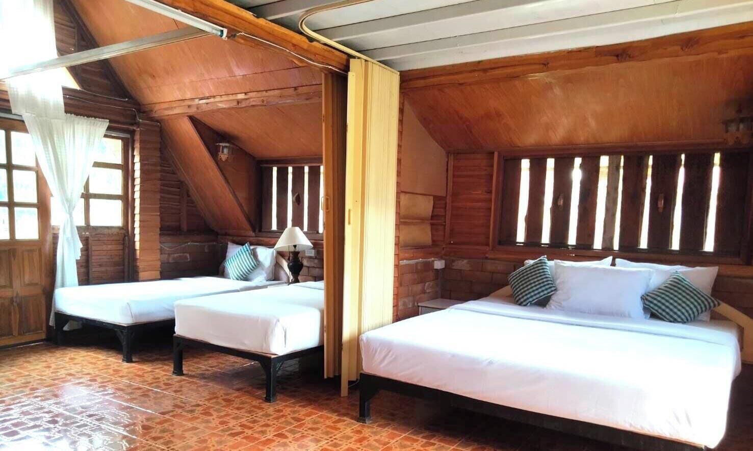 Una cabaña de madera con dos camas, un ventanal con persianas y suelo de baldosas.