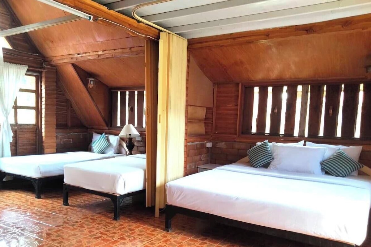 Una cabaña de madera con dos camas, un ventanal con persianas y suelo de baldosas.