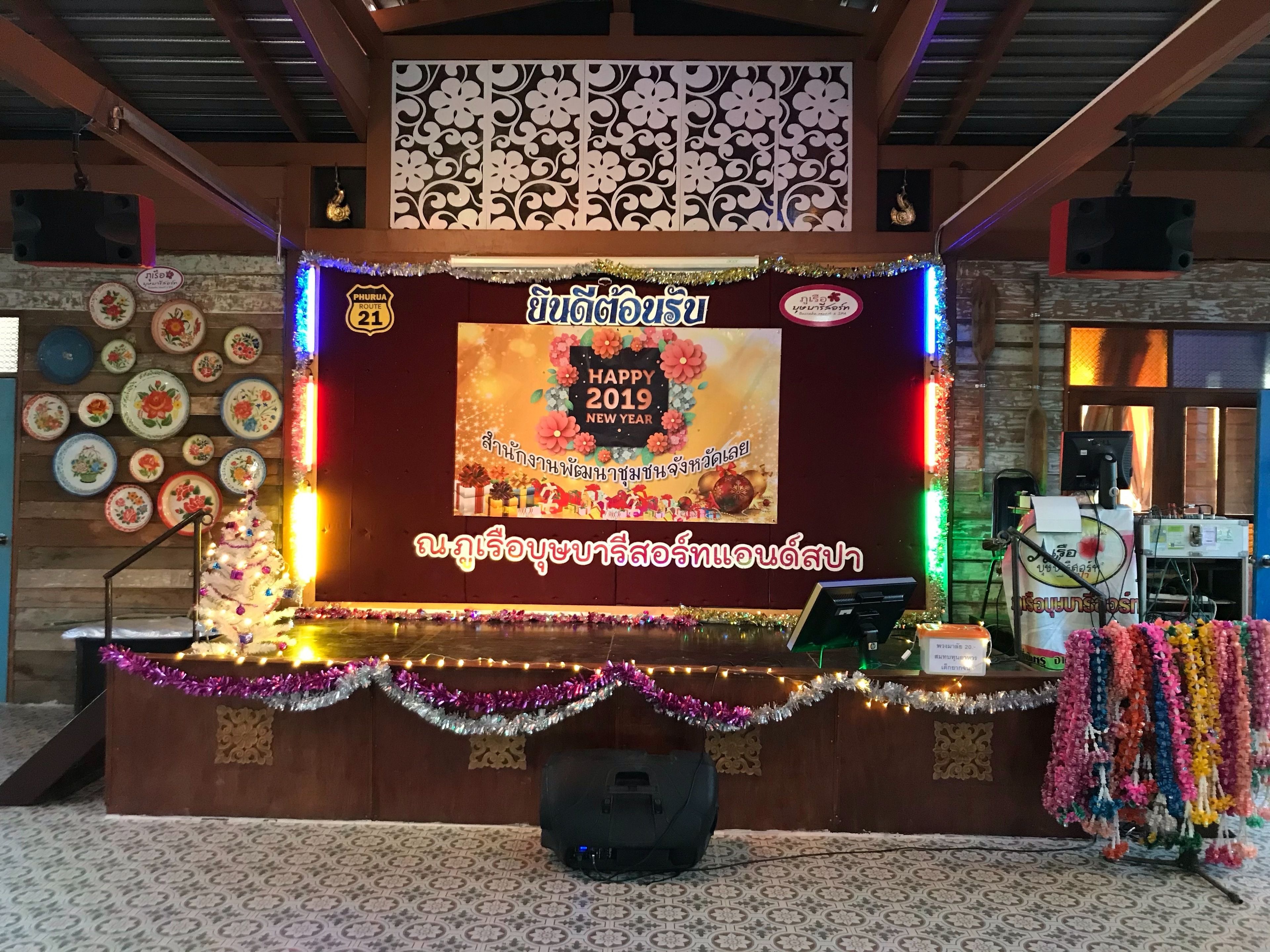 A decorated stage with a 'Happy New Year 2019' sign, surrounded by festive garlands and a Christmas tree.