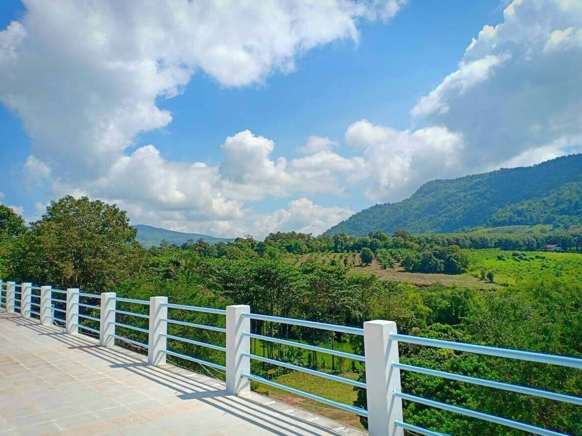 Un sendero pavimentado con barandilla blanca que da vista a un paisaje verde exuberante con árboles y colinas.