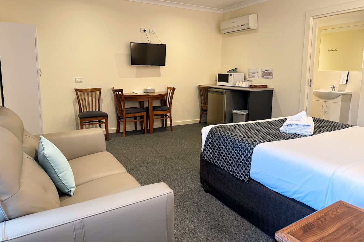 A hotel room with a bed, a sofa, a desk with a computer, a TV, and a bathroom.