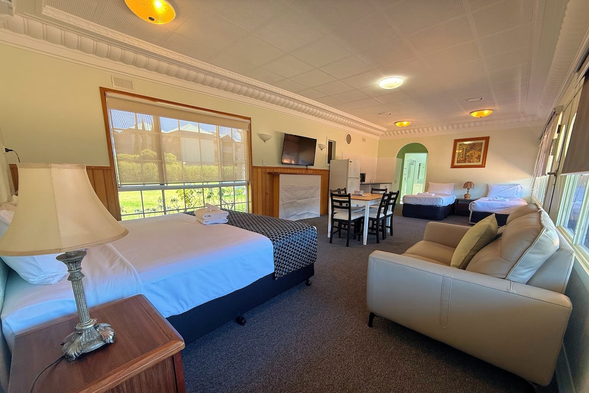 A hotel room with a bed, a sofa, a dining table, and a TV.