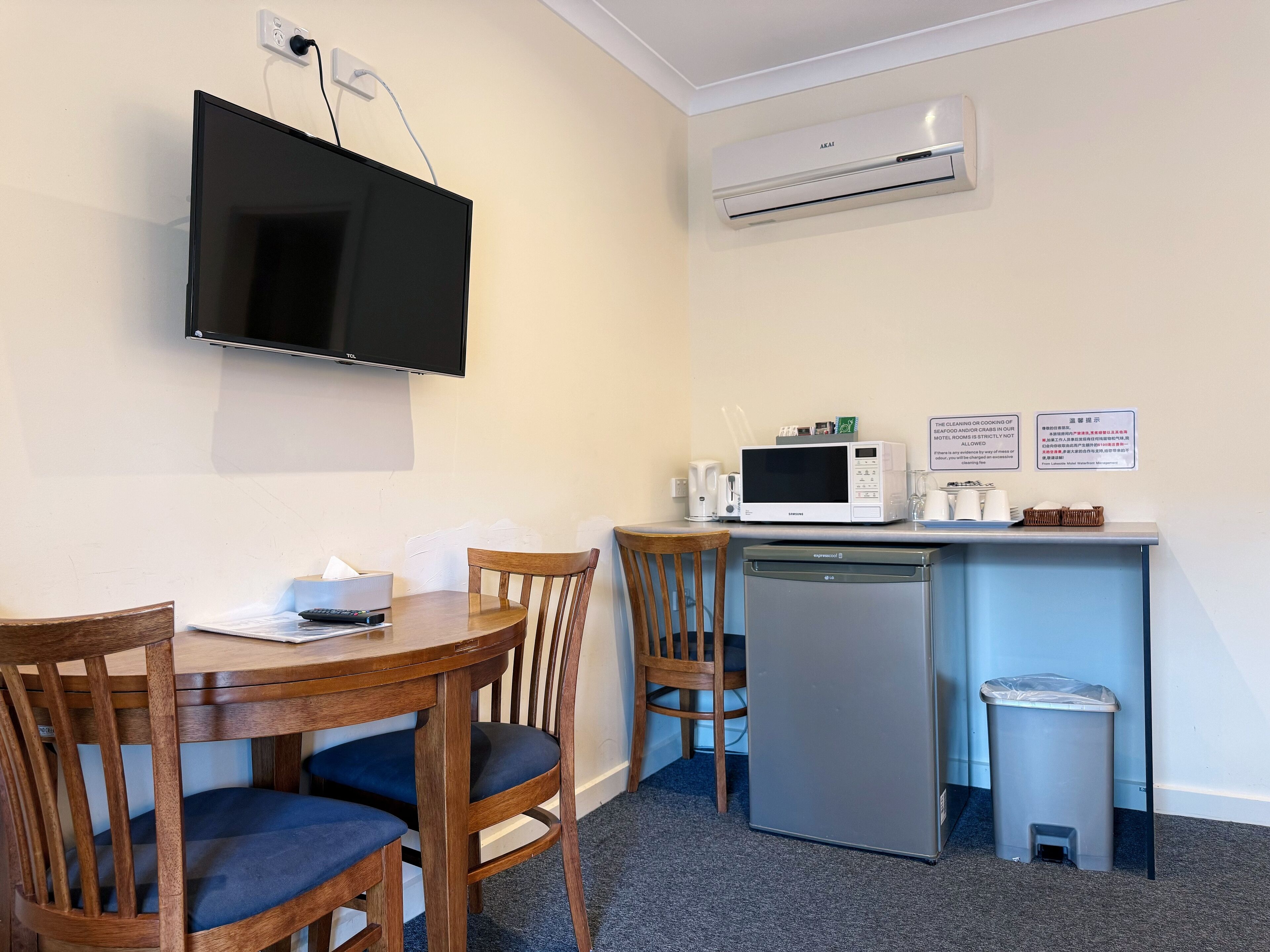 A compact kitchenette with a microwave, a small refrigerator, and a sink. There is a television mounted on the wall and a table with chairs.