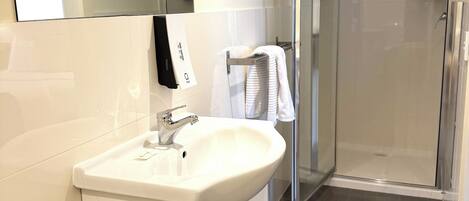 A modern bathroom with a white sink, mirror, and glass shower enclosure.