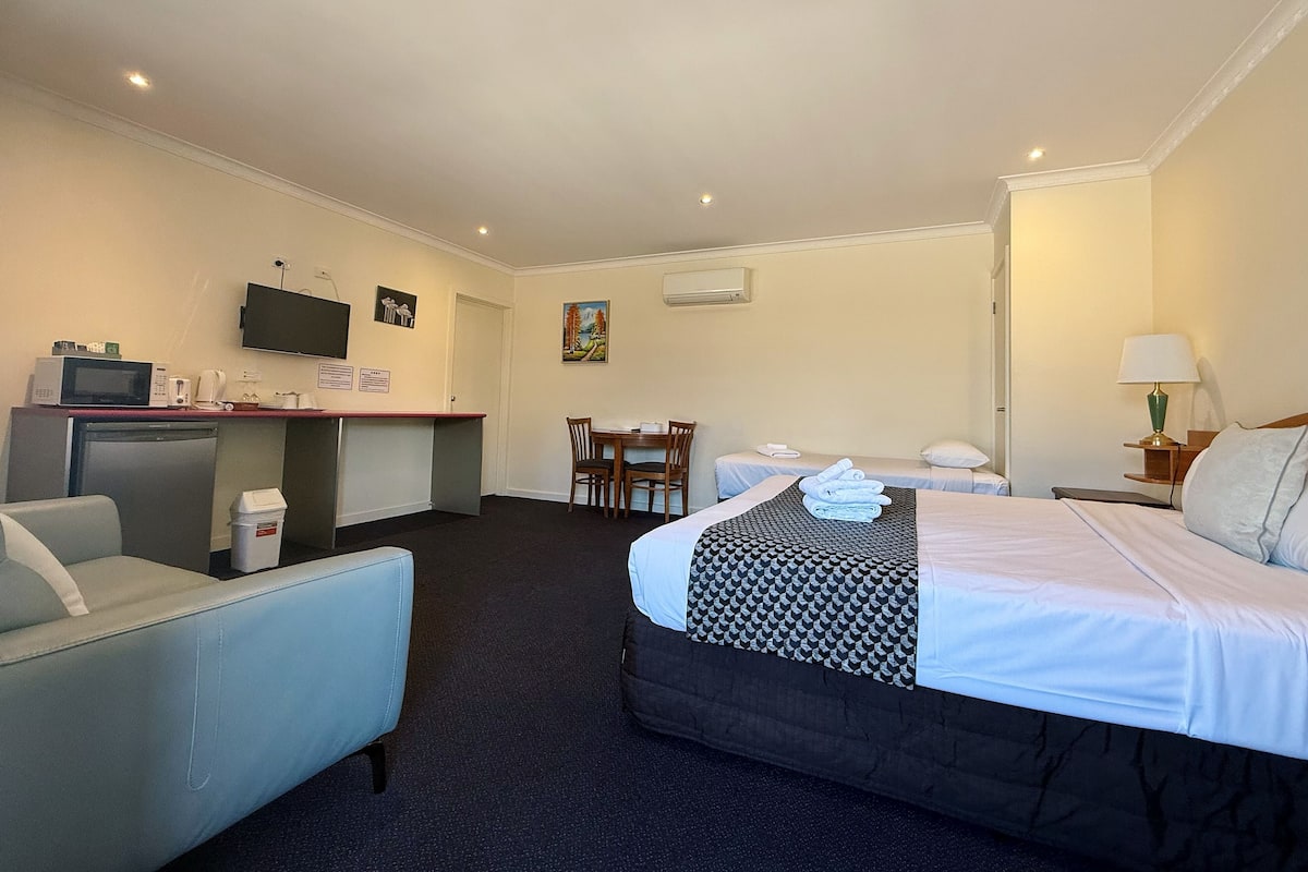A hotel room with a bed, a desk with a computer, a chair, a small table, and a TV on the wall.