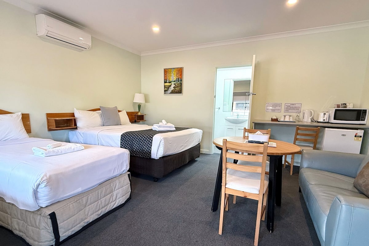 A hotel room with two beds, a dining table, a sofa, a microwave, and a refrigerator.