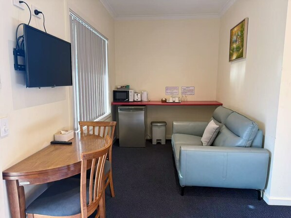 A compact kitchenette with a microwave, toaster, and small refrigerator. There is a dining table with chairs, a sofa, and a television mounted on the wall. - Lakeside Motel Waterfront (Lakes Entrance)