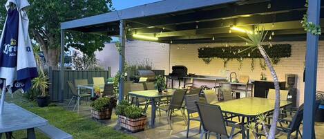 Un patio exterior con zona de estar cubierta, una parrilla y plantas en macetas.
