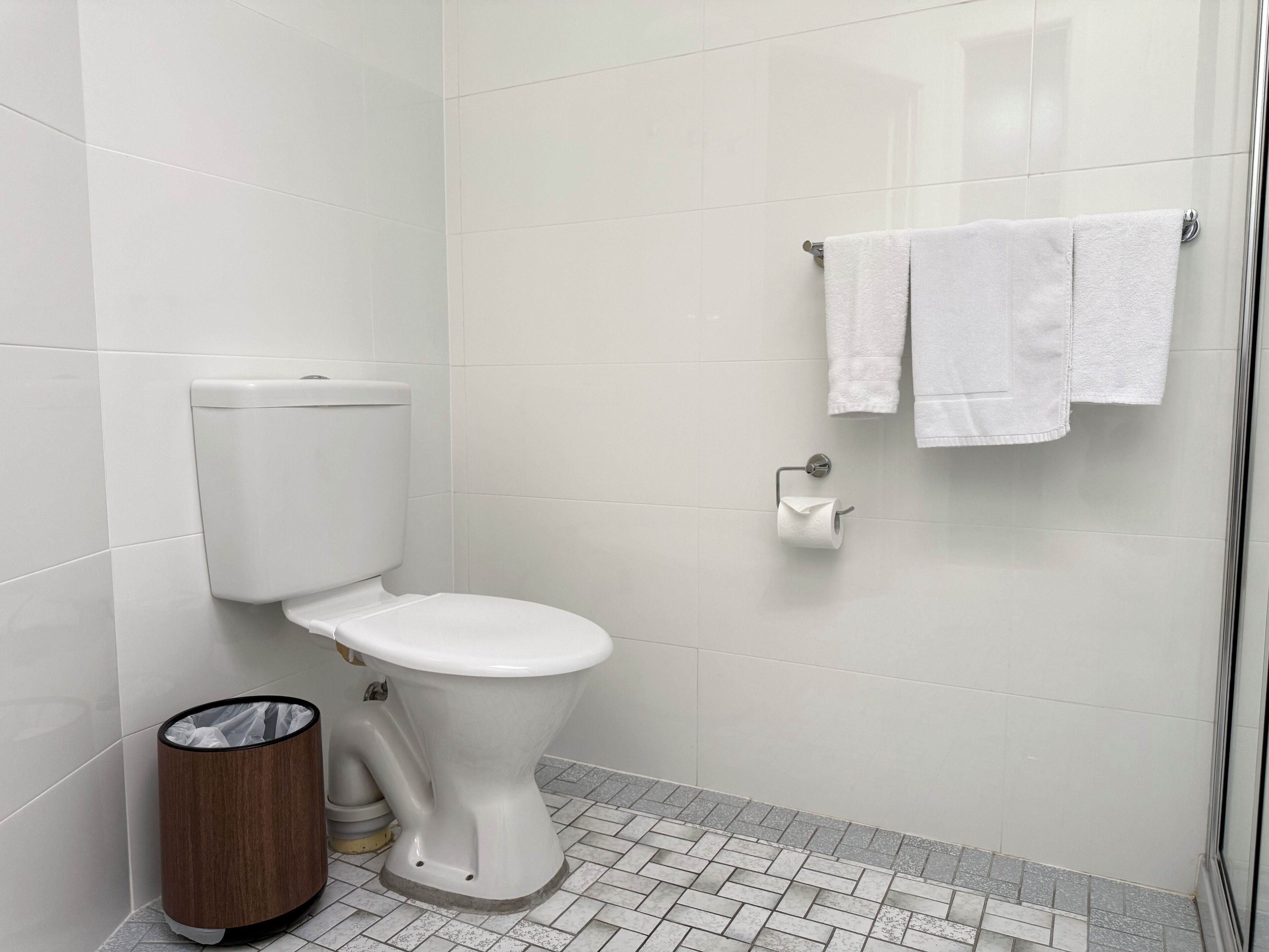 Un baño moderno con inodoro, un cesto de basura y un toallero con dos toallas.