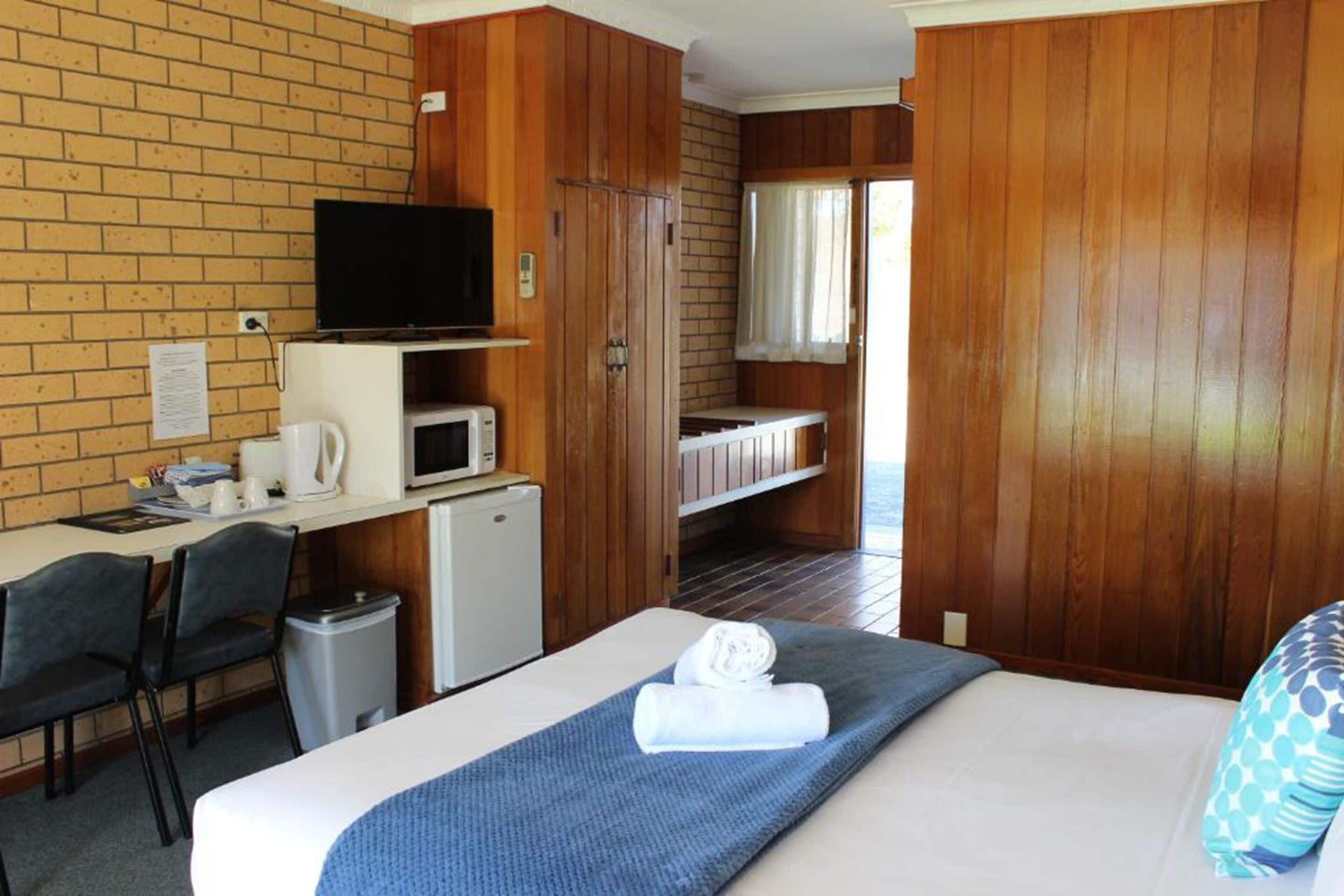 Ett hotellrum med en säng, ett skrivbord med en dator, en tv och ett litet pentry.